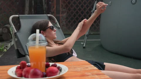 Woman Applying Sunscreen in Backyard with Fresh Fruit and Juice Plate with Stock Footage 345971327