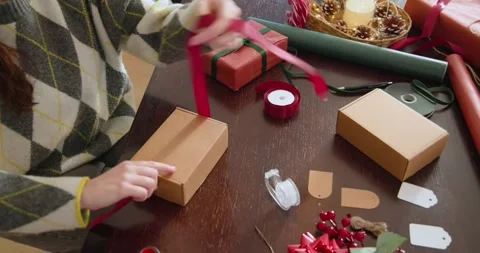 Woman argyle pulling red ribbon tying bow on kraft box at wooden-table wrapping Stock Footage 341953866