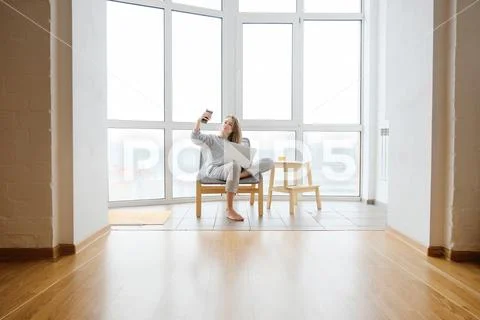 Woman in armchairwith laptop taking selfie on smart phone near panoramic wind Stock Photos