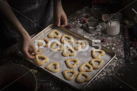 Woman arranging heart shaped biscuits on a baking tray Stock Photos