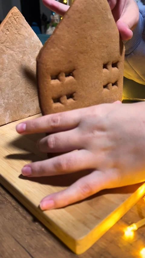 Woman assembles brown gingerbread house, placing wall with white icing Stock Footage 343683664
