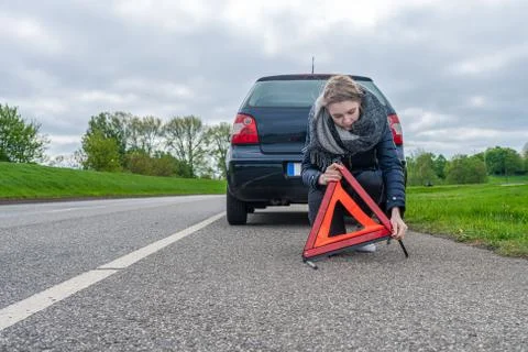 A woman assembles a warning triangle behind the car Stock Photos