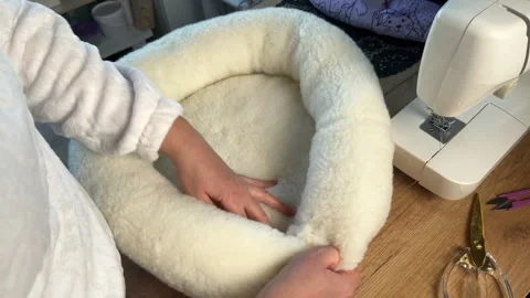 A woman is assembling elements of a pet bed. She is sewing a pet bed from f.. Stockbeeldmateriaal 297081138