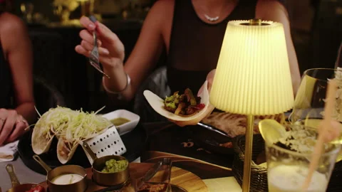 Woman Assembling Tacos at Restaurant Table with Assorted Food and Warm Lighting Stock Footage 342469099