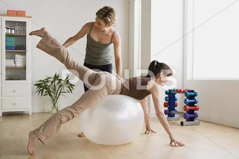 Woman assisting another woman in exercise with fitness ball Stock Photos