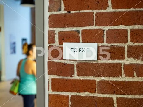 Woman in athletic clothes with in direction of exit sign on brick wall Stock Photos