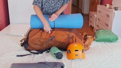 Woman attaching sleeping mat to backpack while preparing camping gear at home Video stock 333471361