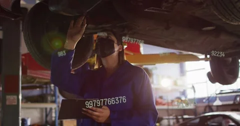 Woman auto tech checking underbody on lift pointing pen causing rising data Stock Footage 330208460