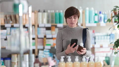 Woman in autumn clothes scans code on cough syrup to check the expiration date Stock Footage 312232743