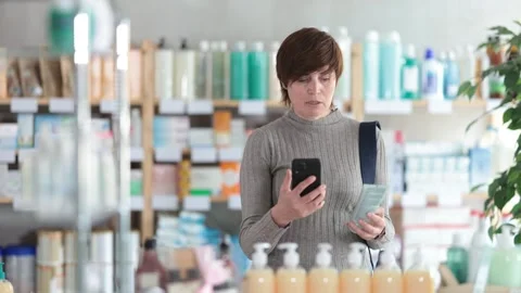 Woman in autumn clothes scans code on package of cream to check the expiration Stock Footage 314243264