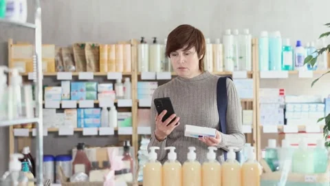 Woman in autumn clothes scans code on package of ointment to check the Stock Footage 318941640