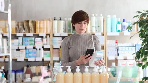 Woman in autumn clothes scans code on package of cream to check the expiration Stockbeeldmateriaal 346643702
