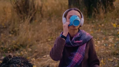 Woman with a backpack drinks tea from a cup, dressed in a brown sweater, holds a Vidéo 255718975