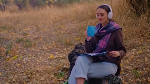 Woman with a backpack drinks tea from a cup, dressed in a brown sweater, holds a 스톡 동영상 255718981