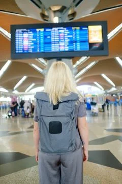 Woman with backpack looking at flight schedule display in a busy airport Foto stock