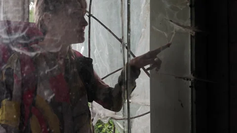Woman with backpack looking at spider web through dirty window of old house Stock Footage 346072631