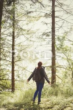 Woman with backpack looking up at trees in sunny woods Stock Photos