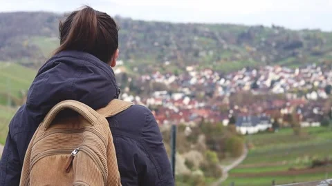 Woman with a backpack stands with her back looking at the panorama of the city Stock Footage 244268016