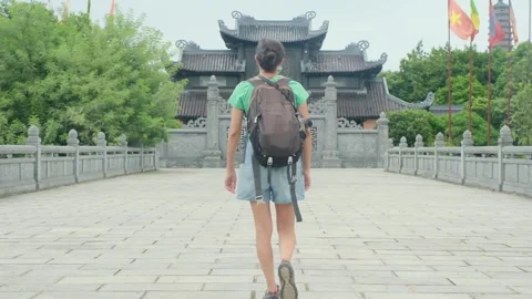 Woman with backpack walking through Southeast Asian temple, capturing culture Stock Footage 248513499