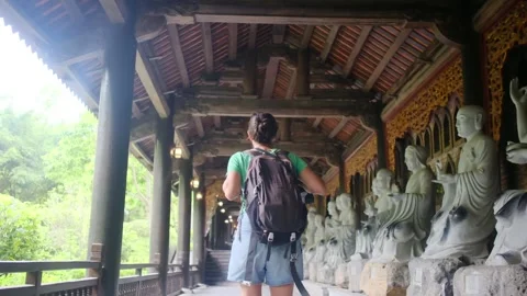 Woman with backpack walking through Southeast Asian temple, capturing culture Stock Footage 248513712