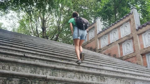 Woman with backpack walking through Southeast Asian temple, capturing culture Stock Footage 248513835