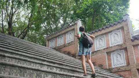 Woman with backpack walking through Southeast Asian temple, capturing culture Stock Footage 248513839