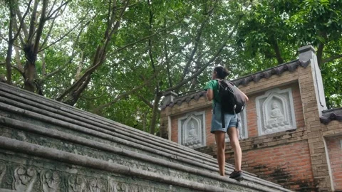 Woman with backpack walking through Southeast Asian temple, capturing culture Stock Footage 248513853