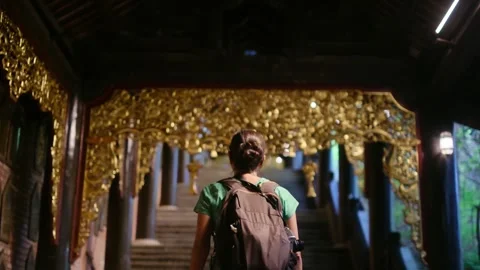 Woman with backpack walking through Southeast Asian temple, capturing culture Stock Footage 248513897