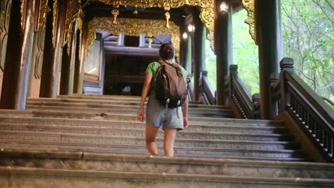 Woman with backpack walking through Southeast Asian temple, capturing culture Stock Footage 248513934