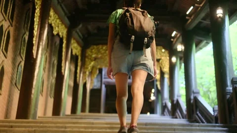 Woman with backpack walking through Southeast Asian temple, capturing culture Stock Footage 248513982