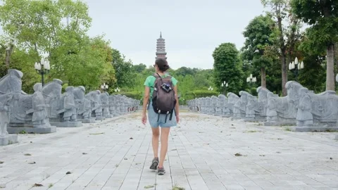 Woman with backpack walking through Southeast Asian temple, capturing culture Stock Footage 248516011