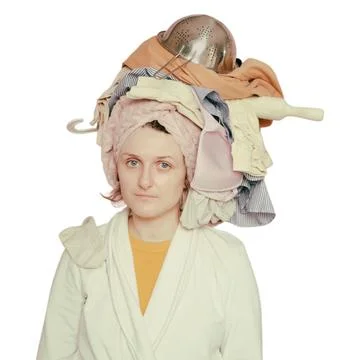 Woman balancing stack of clothes and kitchenware on head. Tired housewife d.. Stockfoto's