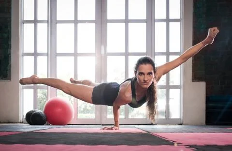 Woman balancing while doing a one hand push up showing strength and determina Stock Photos