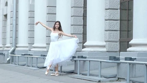 Woman ballerina dances near a light building Stock Footage