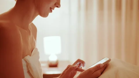 Woman in bath towel using cell phone while resting in bed Stock Footage 165148863