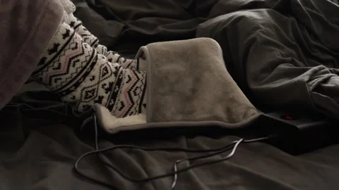 A woman in a bathrobe and patterned woolen socks warms her feet in an electric s Stock Footage 319701138