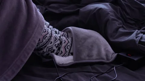 A woman in a bathrobe and patterned woolen socks warms her feet in an electric s Stock Footage 319701246
