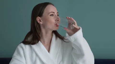 Woman in a bathrobe sitting on the bed drinks clean water of good quality from a Stock Footage 252660341