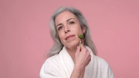 A woman in a bathrobe is using a jade roller on her face Stock Footage 269013555