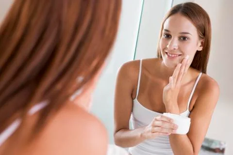 Woman in bathroom applying face cream smiling Stock Photos