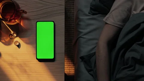 Woman in bed touching green screen of mobile on table Stock Footage 166563939