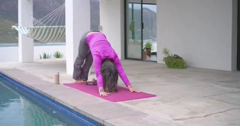 Woman is beginning routine on pink mat by pool, flowing through pushups, rising Stock Footage 341932140