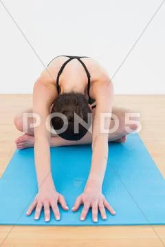 Woman bending while sitting on exercise mat at fitness studio Stock Photos