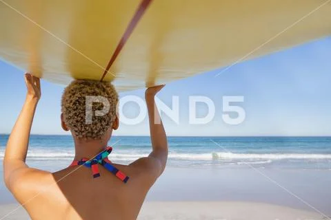 Woman in bikini carrying the surfboard on her head at beach in the sunshine Stock Photos