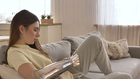 Woman with bionic arm texts message on phone on couch Stock Footage 150242603