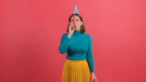 Woman in birthday hat is blowing in pipe, celebrating, on red background. Stock Footage 139691853