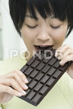 A woman biting into a chocolate bar Stock Photos