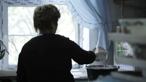 A woman in a black jacket dips a small plate into a black bowl with icing. Stock Footage