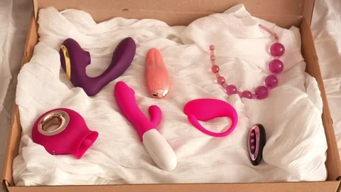 Woman in black transparent glove opens box with pink and purple vibrators and an Stock Footage 319829963