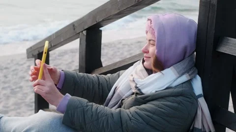 Woman blogger in warm clothes does selphie on the winter beach. Traveller at the Stock Footage 165367853